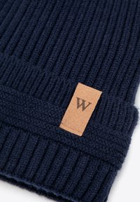 Gorro de punto en azul marino oscuro, con textura acanalada y una parche de cuero color beige con la letra "W". Diseñado para brindar calor y comodidad.