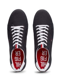 Tênis de lona pretos com atacadores brancos, ilhós prateados e um detalhe em vermelho e branco dentro do colar. Sola de borracha plana.