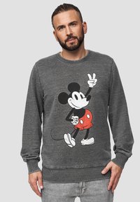 Felpa grigia con una grafica di Topolino in pantaloni rossi con pois bianchi, che fa il segno della pace, con polsini e orlo a coste.