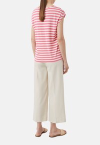 Różowo-biała, w paski, koszulka z krótkim rękawem w luźnym kroju, w zestawieniu z kremowymi, szerokimi spodniami i jasnymi sandałami.