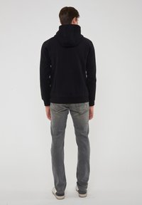 Felpa nera con cappuccio e texture liscia, abbinata a jeans grigio chiaro e scarpe da ginnastica chiare. Cuciture e tasche visibili.