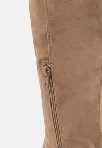 Bota de ante en color marrón claro, de altura hasta la rodilla, con cremallera lateral y costuras en contraste a lo largo de la costura para un detalle y textura añadidos.