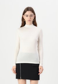 Maglia a collo alto a maniche lunghe in bianco sporco, realizzata in materiale leggero, con una sfumatura che va al grigio chiaro nella parte inferiore.