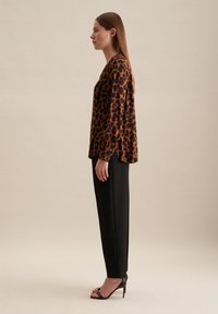 Blusa con stampa leopardata in marrone e nero, abbinata a pantaloni neri su misura e sandali con tacco nero, mostrata di lato.