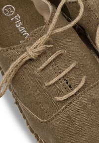 Brown canvas shoes with a textured surface, featuring beige laces and stitching, and a round toe design. Logo visible inside.