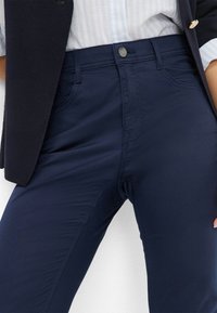 Navyblauwe broek van gladde stof met een knoopsluiting, voorzakken en een getailleerde silhoutte.