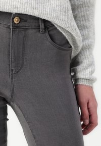 Gray denim jeans with a fitted design, featuring a front button closure, pocket detailing, and smooth texture, paired with a light gray sweater.