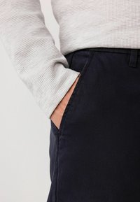 Sivá textúrovaná košeľa s dlhým rukávom a rebrovaným vzorom spolu s námorníckymi nohavicami so bočnou kapsou, ktoré predvádzajú výrazné kontrasty látok.