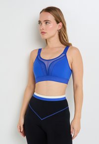 Il reggiseno sportivo blu presenta dettagli in rete, spalline larghe e una vestibilità aderente. Abbinato a leggings neri a vita alta con accenti blu.