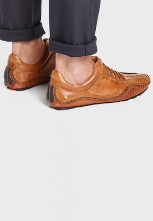 Helle lederschuhe mit glatter Oberfläche und kontrastierender Naht, die eine geschwungene Form und strukturierte Akzente an der Ferse aufweisen.