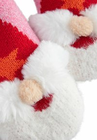 Røde og lyserøde strikkede hjemmesko med fluffy hvide detaljer og pomponer, der har en blød tekstur og stjernemønstre i livlige farver.