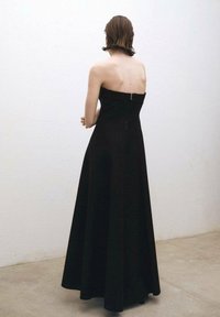 Svart strapless maxiklänning med en figurnära överdel och fladdrande kjol. Har en dragkedja i ryggen och en jämn tygtextur.