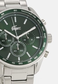 Ceas din oțel inoxidabil cu un cadran verde, accente argintii, trei sub-cadrane, scară tachimetrică și o brățară metalică legată.