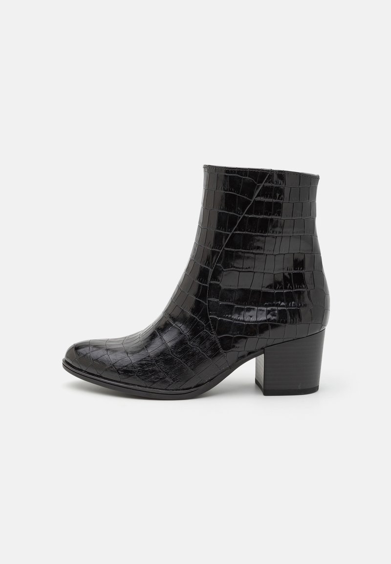 Bottine noire à cheville avec texture crocodile, bout arrondi et talon bloc sur un fond gris clair uni.
