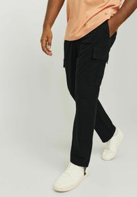 Czarne bojówki z bawełny z bocznymi kieszeniami, zestawione z białymi sneakersami. Strój ma luźny krój i proste elementy designu.