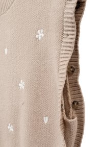 Maglione senza maniche beige con bordi a coste, caratterizzato da fiori ricamati bianchi e dettagli a forma di cuore, con bottoni decorativi sul lato.
