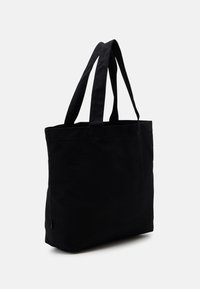 Sac en toile rectangulaire noir avec deux longues poignées, se tenant debout contre un fond blanc uni.