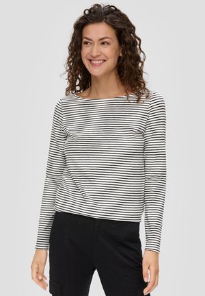 Chemise à rayures noires et blanches à manches longues avec un col bateau, en tissu léger, coupe décontractée, portée avec un pantalon noir.