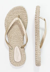 Tong dengan tekstur jerami berwarna beige yang dilengkapi dengan tali emas metalik. Memiliki bentuk bulat dan alas datar. Logo tercetak di bagian bawah.