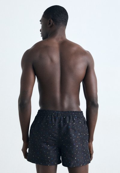 Shorts de bain noirs avec un motif géométrique coloré, taille élastique et poches latérales, fabriqués dans un tissu lisse et léger.