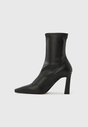 Bota de salto alto preta até ao tornozelo, feita em pele lisa, com biqueira pointed e salto bloco, apresentando um design superior sem costuras em forma de meia.