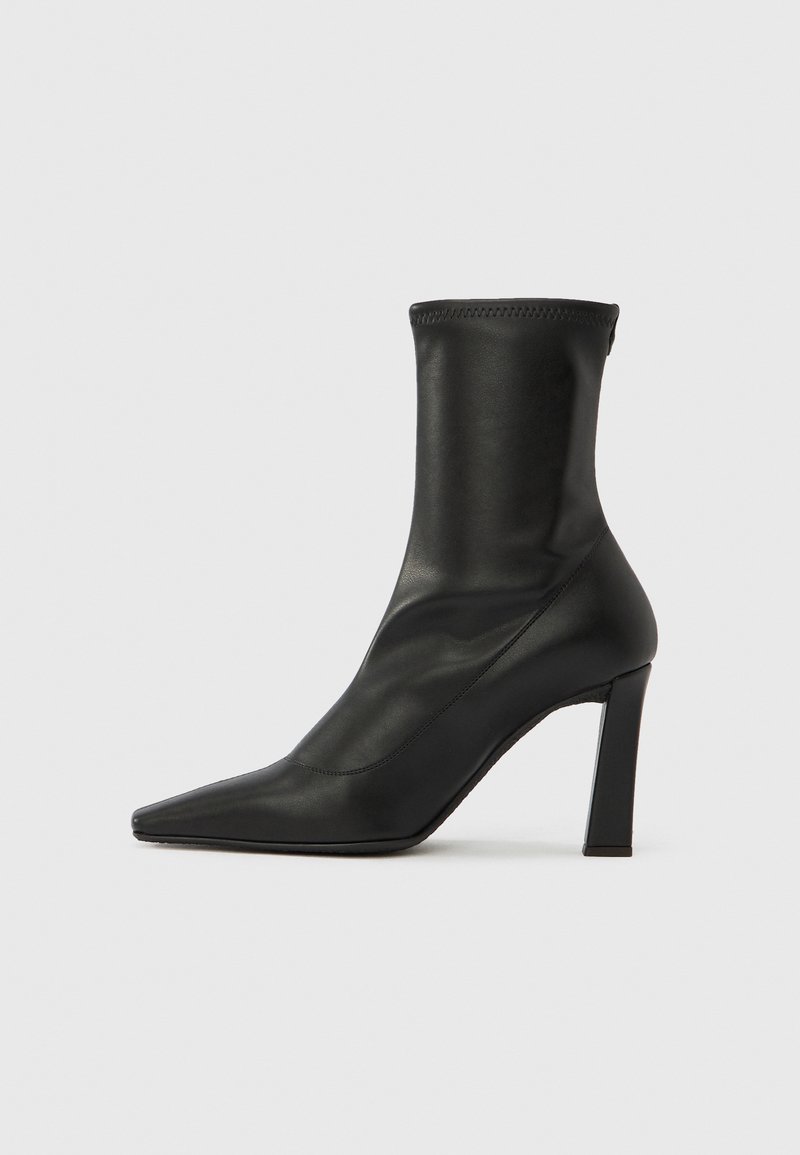 Melns augstpapēžu potīšu zābaks no gludas ādas ar smailu purngalu un bloka papēdi, ar bezšuvju zeķes tipa augšdaļu.