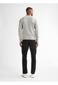 Grijze sweatshirt met geribbelde boorden en onderrand, gecombineerd met zwarte jeans met achterzakken, afgewerkt met witte sneakers.