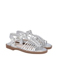 Sandalias gladiadoras plateadas con múltiples correas estrechas, un hebilla ajustable en el tobillo y una suela plana marrón. Textura metálica suave.