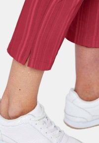 Rote, gerippte, cropped Hose mit seitlichen Schlitzen am Saum, kombiniert mit weißen strukturierten Sneakern. Der Stoff wirkt leicht und atmungsaktiv.