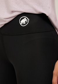 Leggings neri realizzati in tessuto elasticizzato, con un logo bianco di un elefante all'interno di un cerchio sulla vita. La cucitura è visibile.