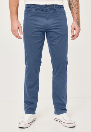 Blaue Baumwoll-Chinos mit geradem Bein, ausgestattet mit Fronttaschen und einem Reißverschluss. Kombiniert mit weißen Sneakern für einen lässigen Look.