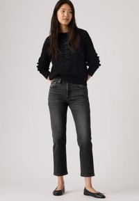 Pulover negru tricotat cu model texturat, asociat cu blugi drepti gri închis și balerini negri. Ținută casual cu accente simple.