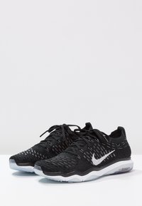 Scarpe da ginnastica nere con tomaia in maglia, caratterizzate da un logo swoosh bianco, un motivo testurizzato e una suola trasparente con accenti grigi.