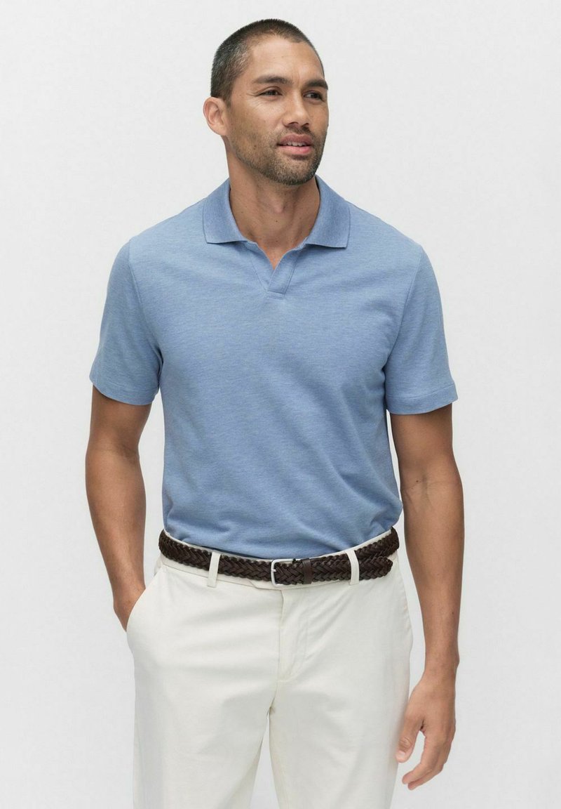 Ljusblå pikétröja av mjukt tyg, med klassisk krage och korta ärmar, i kombination med beige byxor och ett flätat brunt bälte.