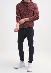 Burgunderfarbener Kapuzenpullover mit strukturiertem Strickdesign, kombiniert mit dunklen Slim-Fit-Jeans und weißen Sport Sneakers.