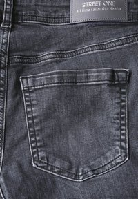 Jean en denim foncé avec une poche arrière de forme rectangulaire. Le tissu a une texture lisse avec des détails de couture subtils.