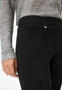 Zwarte sportbroek met zijzakken, met een getextureerde tailleband en een soepele stof. De top heeft een grijze, sprankelende gebreide patroon.
