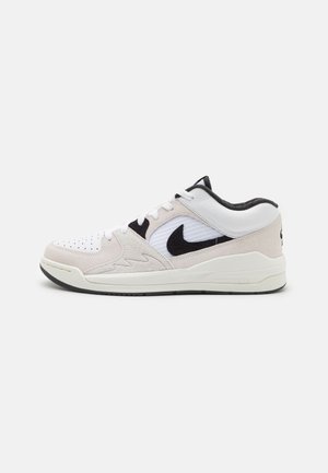Niedrig geschnittene weiße und beige Nike-Sneaker mit schwarzem Swoosh-Logo, weißen Schnürsenkeln und gepolsterter schwarzer Kragen vor einem schlichten weißen Hintergrund.