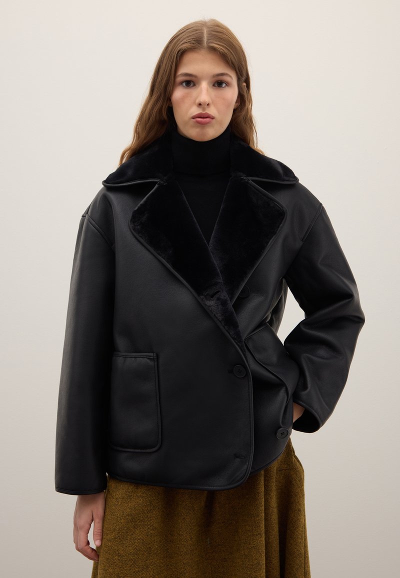 Black faux leather jacket with a wide collar and soft lining, featuring a double-breasted design and side pocket. Smooth texture.