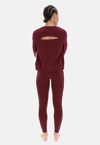 Burgundowy strój fitness składający się z krótkiego swetra z wykrojem w kształcie muszelek z tyłu oraz dopasowanych legginsów z bocznymi akcentami w kształcie muszelek.