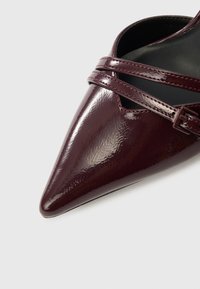 Pantof din piele lacuită burgundă, cu vârf ascuțit, prevăzut cu două bretele încrucișate și o mică cataramă pentru fixare sigură.