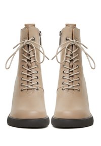 Bottines beiges en cuir à lacets avec semelles noires et fermetures éclair latérales, vues de face avec les lacets noués en nœuds.