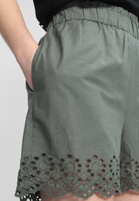 Shorts en coton vert avec une taille élastique, des poches latérales et un ourlet festonné orné d'un délicat tissu ajouré brodé.
