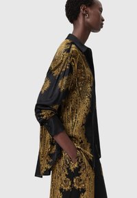 Black silk shirt featuring intricate gold baroque patterns, button cuffs, and a relaxed fit, styled with a matching patterned bottom.