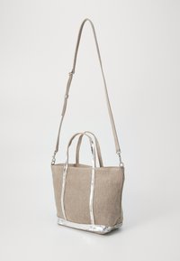 Bež torba od platna s srebrnim metalnim obrubom, dvostrukim gornjim ručkama i podesivim remenom za rame. Kutijasti oblik s teksturiranom površinom.