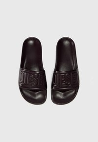 Black slide sandals with a wide strap featuring embossed "DIESEL" logo. Made of soft rubber-like material with a smooth texture and rounded shape.
