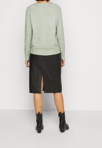 Ljusgrön tröja med texturerad yta och ribbad fåll, i kombination med en svart läderkjol med bakslits och svarta ankelstövlar.