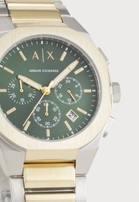 Grünes Zifferblatt mit einem Band aus goldfarbenem und silbernem Edelstahl. Verfügt über Chronographen-Subzifferblätter, Datumsanzeige und auffällige Markierungen für die Uhrzeit.