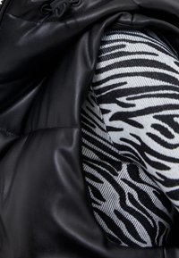 Das Innere einer schwarzen Lederjacke mit einem weißen und schwarzen Zebra-Print-Futter. Weiche Textur und glatte Oberfläche der äußeren Schicht.