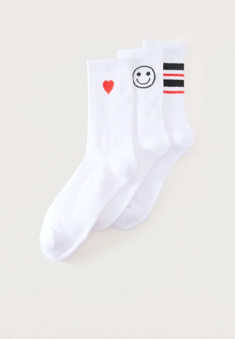 Trois chaussettes blanches montantes avec des bords côtelés, ornées d’un cœur rouge, d’un smiley noir et blanc, et de rayures horizontales noires et rouges.